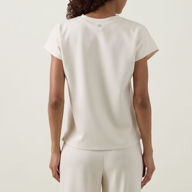 Model wearing Joseph Ribkoff Relaxed Scuba Top in Birch, rear view, short sleeves, relaxed fit, styled with matching wide-leg trousers
