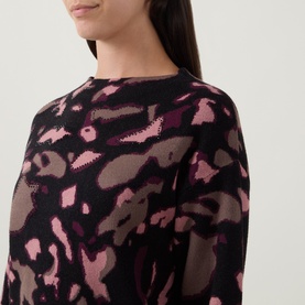Model wearing Joseph Ribkoff Abstract Print Embellished Sweater in black and pink abstract print, featuring boat neckline and long sleeves.