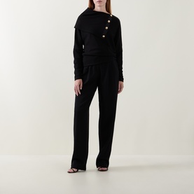 Model wearing Joseph Ribkoff black top with asymmetric neckline and gold-tone buttons, styled with matching black wide-leg trousers and heeled