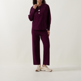 Model wearing Joseph Ribkoff Rib Knit Button Sweater in Elderberry with matching wide-leg knit trousers and beige trainers.