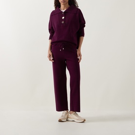 Model wearing Joseph Ribkoff Rib Knit Button Sweater in Elderberry with matching wide-leg knit trousers and cream trainers.