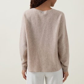 Model wearing Joseph Ribkoff cashmere top in Oatmeal Melange, back view, relaxed fit with dropped shoulders, styled with white trousers.