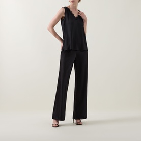 Model wearing Joseph Ribkoff black sleeveless satin top with lace trim neckline, styled with wide-leg black trousers and heeled sandals.
