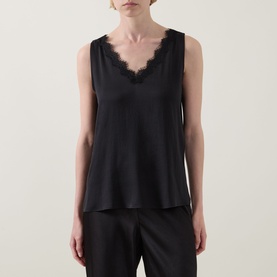 Model wearing Joseph Ribkoff black sleeveless top with lace-trimmed V-neckline, styled with black wide-leg trousers.