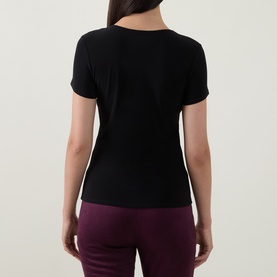 Model wearing Joseph Ribkoff Solid Fitted T-Shirt in black, rear view, crew neck, short sleeves, straight hem, styled with burgundy trousers.