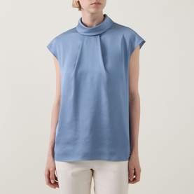 Model wearing Joseph Ribkoff Chambray Top in light blue with draped mock neck and cap sleeves, styled with white trousers.