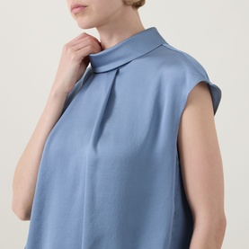 Model wearing Joseph Ribkoff Top in chambray blue, featuring a folded mock neck and sleeveless cut in a relaxed silhouette.
