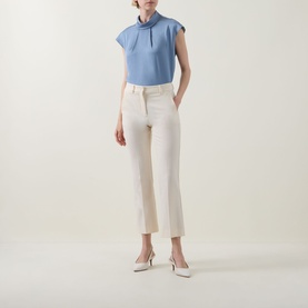 Model wearing Joseph Ribkoff Chambray Top in blue with cap sleeves and keyhole neck, styled with cream trousers and white heels.