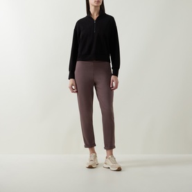 Model wearing Joseph Ribkoff Sporty Half-Zip Sweatshirt in black with shawl collar, styled with mauve tapered trousers and cream trainers.