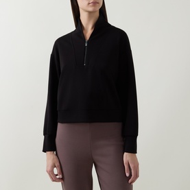 Model wearing Joseph Ribkoff Sporty Half-Zip Sweatshirt in black with shawl collar, styled with mauve trousers.