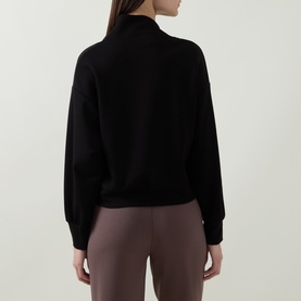 Model wearing Joseph Ribkoff Sporty Half-Zip Sweatshirt in black, shown from behind, styled with mauve trousers.