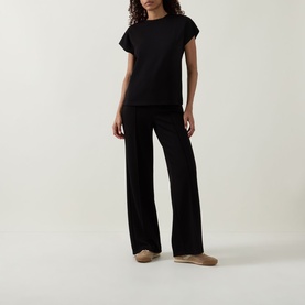 Model wearing Joseph Ribkoff Wide Leg Scuba Trousers in black with elasticated waist, styled with a black cap-sleeve top and nude flats.
