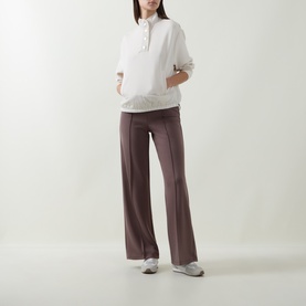 Model wearing Joseph Ribkoff Mink wide-leg trousers with front seam detail, styled with a white half-zip pullover and grey trainers.