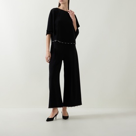 Model wearing Joseph Ribkoff Beaded Wide Leg Culottes Trousers in black with faux pearl trim, styled with a matching black top and heels.