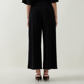 Model wearing Joseph Ribkoff Beaded Wide Leg Culottes Trousers in black with faux pearl hem detail, styled with black heeled sandals. Rear view.