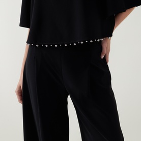 Model wearing Joseph Ribkoff Beaded Wide Leg Culottes Trousers in black with faux pearl beaded waistband detail, styled with matching black top.