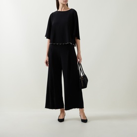 Model wearing Joseph Ribkoff Beaded Wide Leg Culottes Trousers in black with faux pearl waist detail, styled with black top and heels.