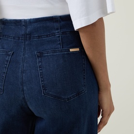 Model wearing Joseph Ribkoff dark denim blue jeans, close-up of back pockets with gold brand tab detail, white top styled with.
