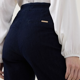 Model wearing Joseph Ribkoff dark denim blue high-waisted trousers with gold logo tab, styled with a white blouse.