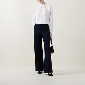 Model wearing Joseph Ribkoff dark denim blue wide-leg trousers, styled with a white blouse and black heels, carrying a small black shoulder bag.