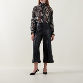Model wearing Joseph Ribkoff black wide-leg cropped trousers in faux leather finish, styled with animal-print blouse and black heels.