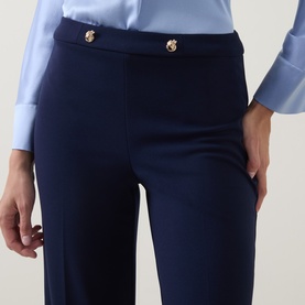 Model wearing Joseph Ribkoff indigo trousers with gold-tone button waist detail, styled with a light blue shirt.