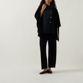 Model wearing Joseph Ribkoff black trousers styled with a black quilted jacket, cape and flat loafers.