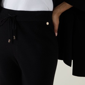 Model wearing Joseph Ribkoff black trousers with drawstring waist, side pockets, and rose gold logo charm detail.