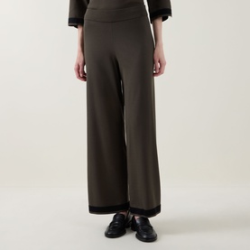 Model wearing Joseph Ribkoff wide-leg trousers in avocado and black, with contrast trim at waist and hem, paired with black loafers.