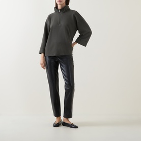 Model wearing Joseph Ribkoff black faux leather slim-leg trousers, styled with a dark khaki half-zip sweatshirt and black flat loafers.