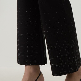 Model wearing Joseph Ribkoff Embellished Flared-Leg Trousers in black with rhinestone dot detailing, shown from knee to hem with strappy heels.