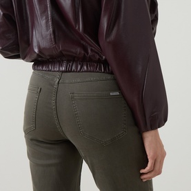 Model wearing Joseph Ribkoff Slim-Leg Jeans in Avocado, five-pocket styling with logo detail, paired with a burgundy leather jacket.