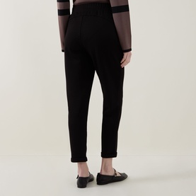 Model wearing Joseph Ribkoff black tapered trousers, back view, styled with a sheer stripe top and black flat shoes.