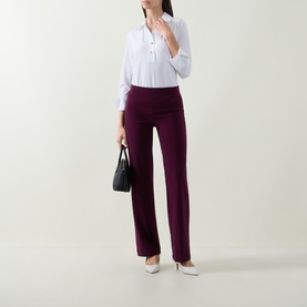 Model wearing Joseph Ribkoff elderberry wide-leg trousers, styled with a white shirt and cream heels, carrying a black handbag.