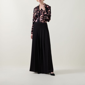 Model wearing Joseph Ribkoff black wide-leg trousers with pleated front, styled with a floral print blouse and black heels.