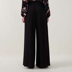 Model wearing Joseph Ribkoff black wide-leg trousers, styled with a floral print blouse, rear view showing fluid drape and full length.