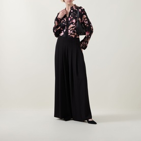 Model wearing Joseph Ribkoff black wide-leg trousers with pleated waist, styled with a floral print blouse and black pointed flats.