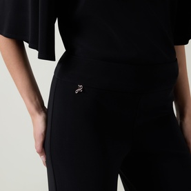 Model wearing Joseph Ribkoff black trousers, close-up of hip area showing logo pin detail, styled with black top.