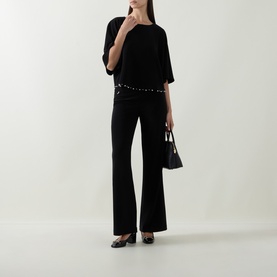 Model wearing Joseph Ribkoff black flared trousers with a black embellished top, carrying a small black bag, styled with black heels.