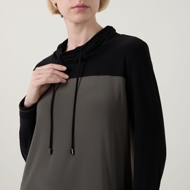 Model wearing Joseph Ribkoff Tunic in Avocado and Black, colour-block hoodie style with drawstring neckline and long sleeves.