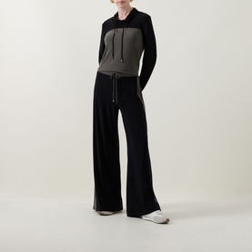 Model wearing Joseph Ribkoff Avocado/Black colour-block hooded tunic with wide-leg black trousers and white trainers.