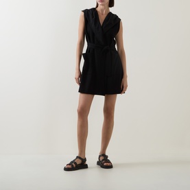 Model wearing Joseph Ribkoff black sleeveless wrap vest styled with a mini skirt and black strappy sandals