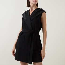 Model wearing Joseph Ribkoff black sleeveless hooded vest with tie belt and front pockets, styled as a dress
