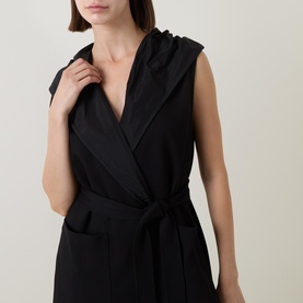 Model wearing Joseph Ribkoff black sleeveless hooded vest with wrap front, tie belt, and side pockets.