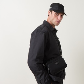 Model with Prada Cappelli Triangle Logo Cap in Nero nylon, curved visor, worn with black shirt; model also carries a black crossbody bag