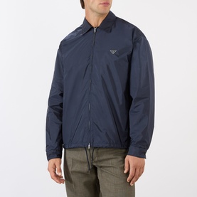 Model wearing Prada Triangle Logo Zip Overshirt in blue Re-Nylon, classic collar, chest logo plaque, styled with khaki trousers.