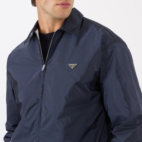 Model wearing Prada Triangle Logo Zip Overshirt in blue Re-Nylon, with gold triangle logo plaque on chest and classic collar