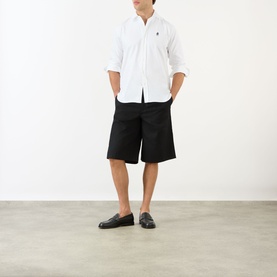 Model wearing Prada Crest Logo Oxford Shirt in white with embroidered logo, styled with black shorts and black loafers.