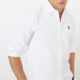 Model wearing Prada Crest Logo Oxford Shirt in white, featuring embroidered crest logo, pointed collar and long sleeves with rolled cuffs.