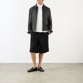 Model wearing Prada Crest Logo Oxford Shirt in white with black harrington jacket, black shorts and black loafers.